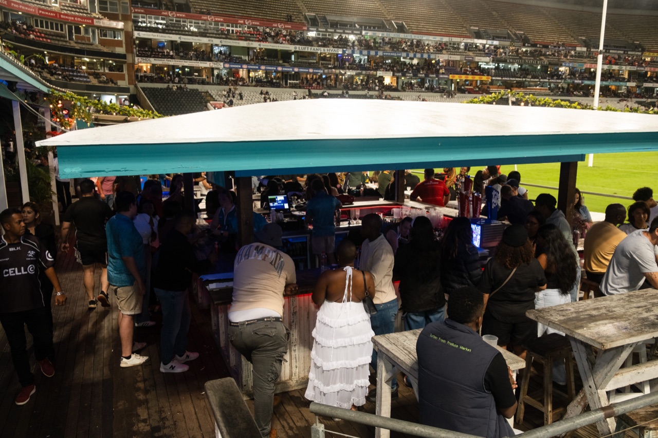 The crowd under the teal awning with the pitch beyond